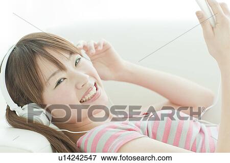 Stock Photo - Young woman listening to music on sofa. Fotosearch