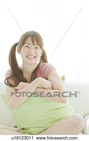 Stock Image - Young woman sitting on sofa. Fotosearch