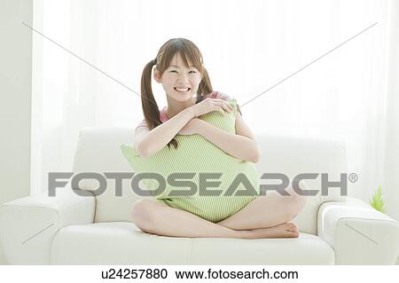 Stock Image - Young woman sitting on sofa. Fotosearch