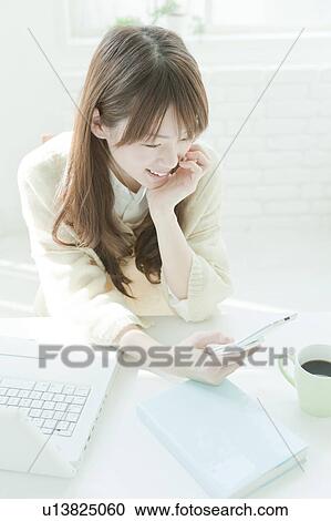 Stock Image - Young woman text messaging at desk. Fotosearch