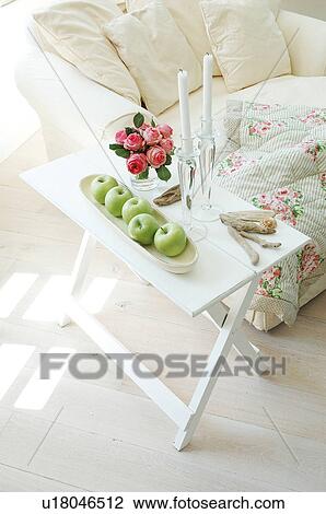 Stock Image - Armchair and folding table with apples, flowers and candles. Fotosearch