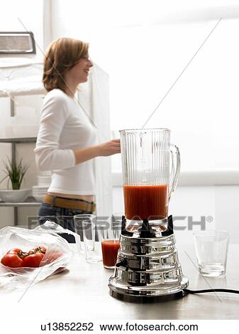 Stock Image - Blender with tomato juice with woman in background. Fotosearch