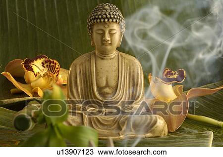 Stock Image - Buddha statuette with blossoms and smoke. Fotosearch