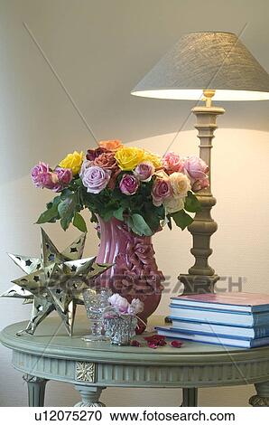 Stock Image - Bunch of flowers, table lamp, decorative star and books on table. Fotosearch