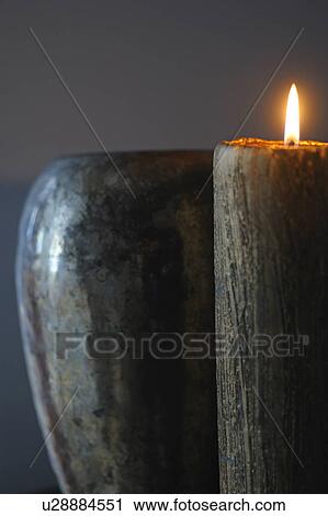 Stock Image - Burning candle in front of vase. Fotosearch