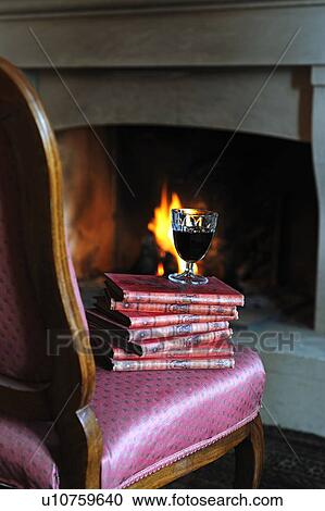 Stock Image - Glass of red wine on stack of books by the fireplace. Fotosearch