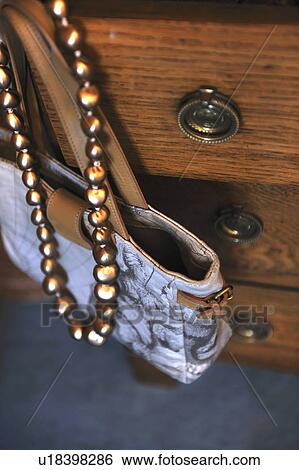 Stock Photograph - Handbag and necklace hanging at dresser. Fotosearch