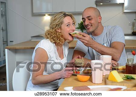 Stock Photo - Happy couple having breakfast in kitchen. Fotosearch