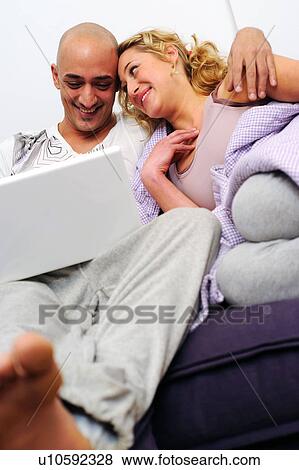Happy couple on couch using laptop View Large Photo Image Stock Photo - Happy couple on couch using laptop. Fotosearch