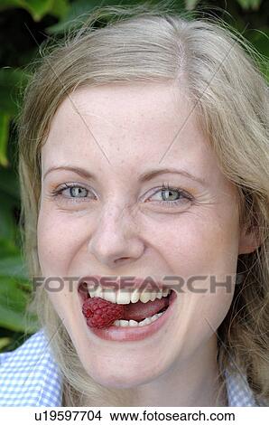 Picture - Happy young woman eating raspberry. Fotosearch