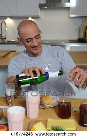 Stock Photograph - Man in kitchen pouring champagne into glass. Fotosearch