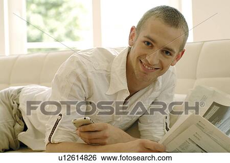 Stock Photograph - Man with cell phone and newspaper on couch. Fotosearch