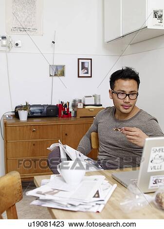Stock Image - Man with newspaper and laptop having breakfast. Fotosearch