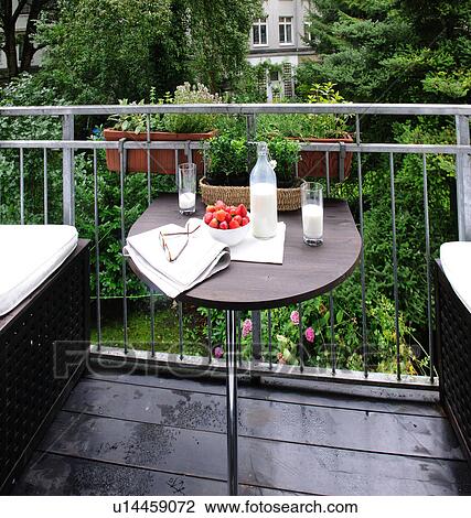 Stock Image - Milk, strawberries, eyeglasses and newspaper on balcony table. Fotosearch