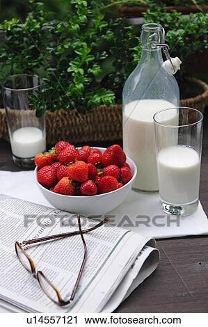 Stock Image - Milk, strawberries, eyeglasses and newspaper on table. Fotosearch