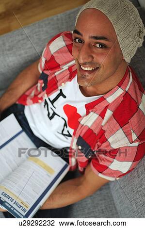 Smiling man holding book sitting on couch View Large Photo Image Stock Image - Smiling man holding book sitting on couch. Fotosearch