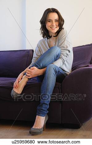 Stock Image - Smiling young woman sitting on sofa. Fotosearch