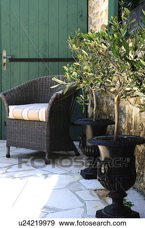 Stock Photo - Two flower pots and wicker chair on terrace of a country house. Fotosearch