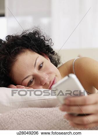 Stock Photograph - Woman looking at cell phone in bed. Fotosearch