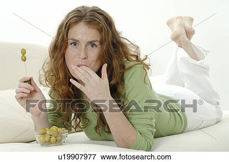 Stock Photo - Woman lying on couch eating olives. Fotosearch