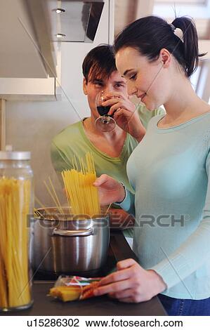 Stock Image - Young couple in kitchen cooking spaghetti and drinking red wine. Fotosearch