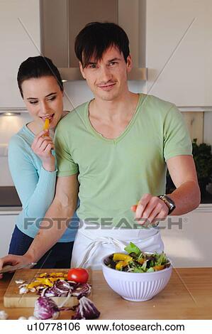 Stock Photograph - Young couple in kitchen preparing salad. Fotosearch