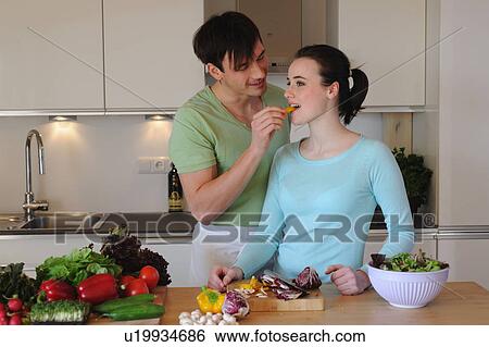 Stock Photograph - Young couple in kitchen preparing salad. Fotosearch