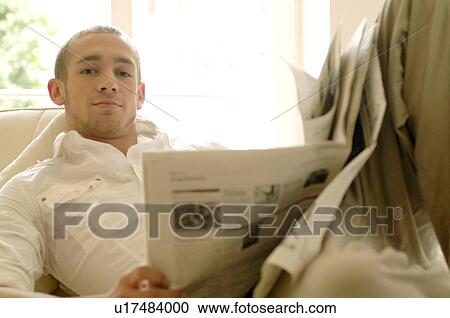 Young man reading newspaper on couch View Large Photo Image Stock Image - Young man reading newspaper on couch. Fotosearch
