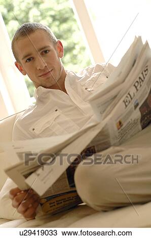 Young man reading newspaper on couch View Large Photo Image Stock Image - Young man reading newspaper on couch. Fotosearch