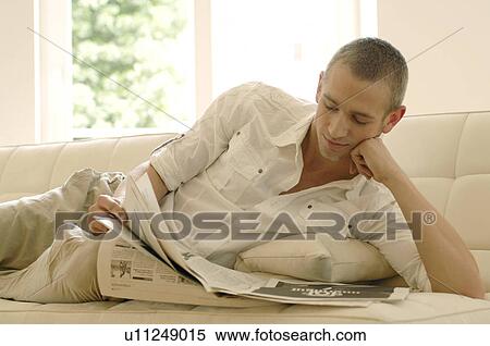 Stock Photography - Young man reading newspaper on couch. Fotosearch