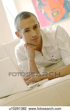 Young man using laptop on couch View Large Photo Image Stock Image - Young man using laptop on couch. Fotosearch