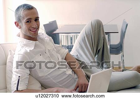 Young man using laptop on couch View Large Photo Image Stock Image - Young man using laptop on couch. Fotosearch