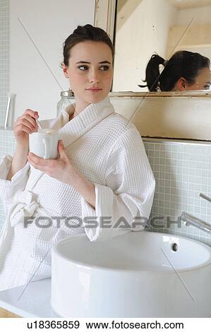 Stock Photo - Young woman drinking coffee in bathroom. Fotosearch