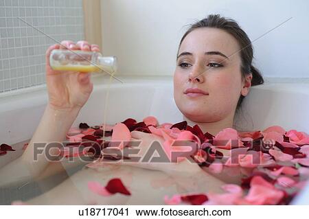 Stock Image - Young woman enjoying bath with rose petals. Fotosearch