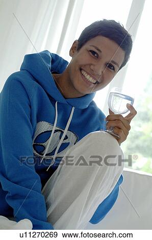 Stock Photo - Young woman holding glass of water on couch. Fotosearch