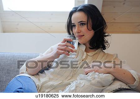 Young woman on couch drinking glass of water View Large Photo Image Stock Photography - Young woman on couch drinking glass of water. Fotosearch