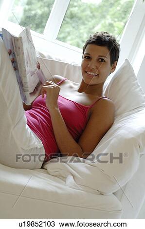 Young woman reading magazine on couch View Large Photo Image Stock Image - Young woman reading magazine on couch. Fotosearch