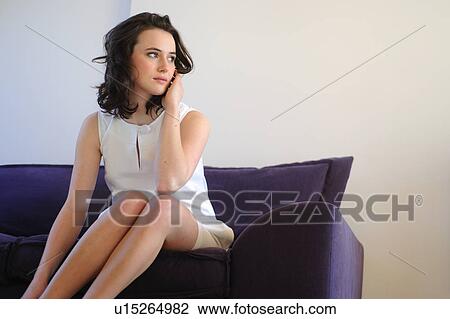 Stock Image - Young woman sitting on sofa. Fotosearch