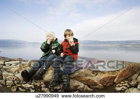 Stock Photo - 2 boys eating fruit at lake. Fotosearch