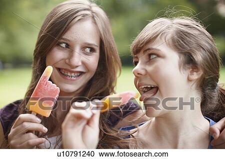 Stock Image - 2 girls eating popsicles together. Fotosearch