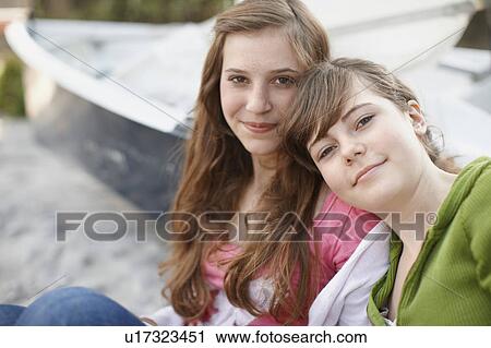 Stock Image - 2 girls sitting together at the beach. Fotosearch