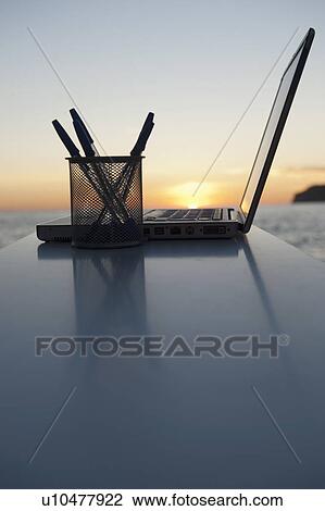 Stock Image - A laptop with a sun setting behind. Fotosearch