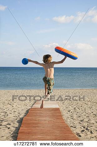 Stock Image - Boy (8-9) running down boardwalk to sea. Fotosearch