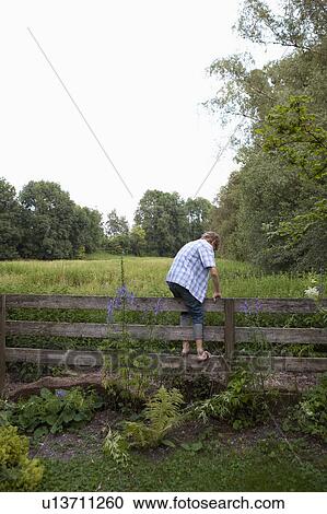 Stock Image - Boy climbing over fence. Fotosearch