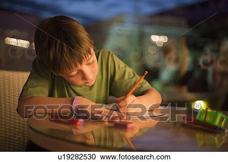 Stock Image - Boy concentrating on writing homework. Fotosearch