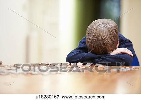 Stock Photo - Boy head on arms surrounded by coins. Fotosearch