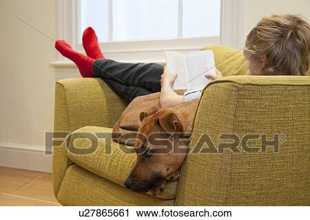 Stock Image - Boy in armchair reading and cuddling dog. Fotosearch