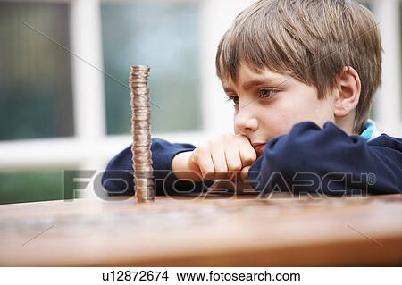 Picture - Boy looking at a tower of coins. Fotosearch