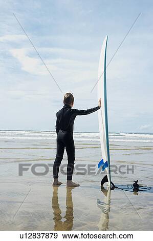 Boy looking out to sea with surf board View Large Photo Image Stock Photo - Boy looking out to sea with surf board. Fotosearch