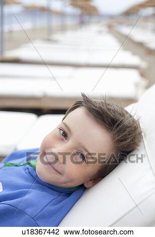 Stock Image - Boy lying on sunlounger on beach. Fotosearch